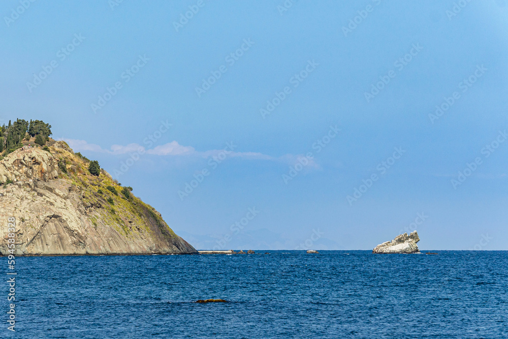 View of calm blue sea. Coastline with cliffs and mountains overgrown with evergreens. Turquoise sea water merges with horizon and turns into blue cloudless sky. Nature concept for design