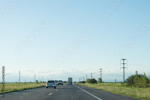 vehiculos viajando por una autopista al atardecer con arbustos y torres de alta tension electrica a los costados, durante el atardecer con nubes en el horizonte, con espacio de copy paste en el cielo photo