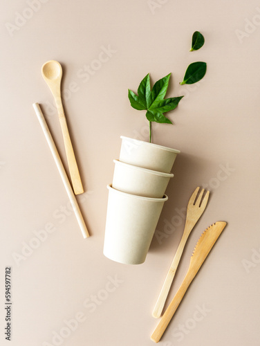 Pappbecher, Bambus Besteck und ein Strohhalm auf einem beigen Tisch. Umwelt, nachhaltige Lebensweise.