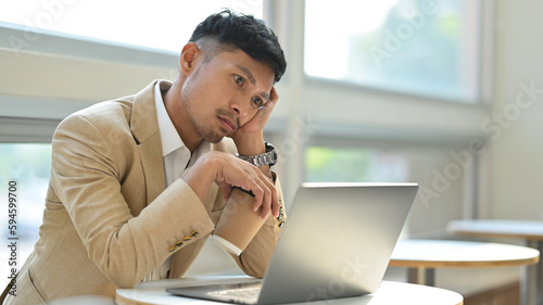 Distracted millennial businessman thinking and looking at laptop screen, boring routine monotonous