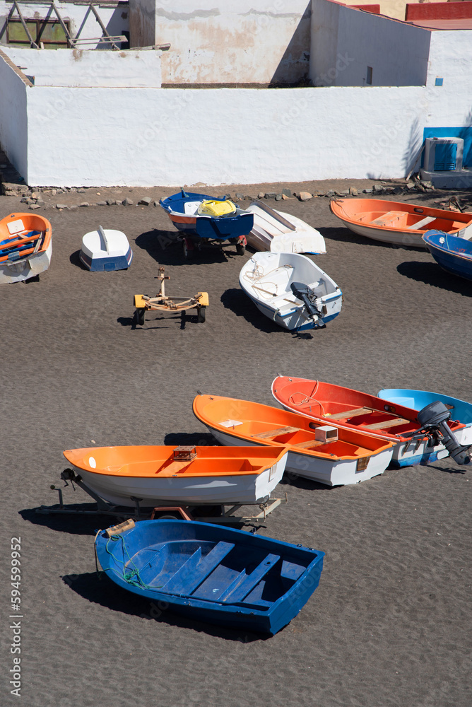 Plano de detalle de coloridos barcos de pesca en la arena negra de la playa en el pueblo de Ajuy en Fuerteventura y en el fondo una fachada blanca típica de la arquitectura de las Islas Canarias.