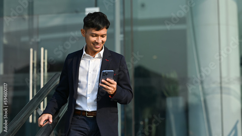Handsome millennial man worker using smartphone while walking outside office building. Modern lifestyle, business, technology concept