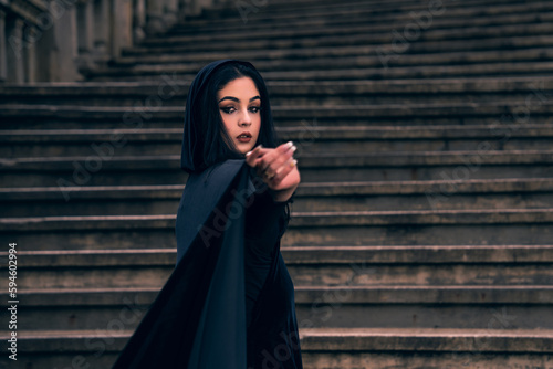 a woman in a black dress standing on a set of stairs with her hands in her pockets and her eyes closed, a matte painting, gothic art