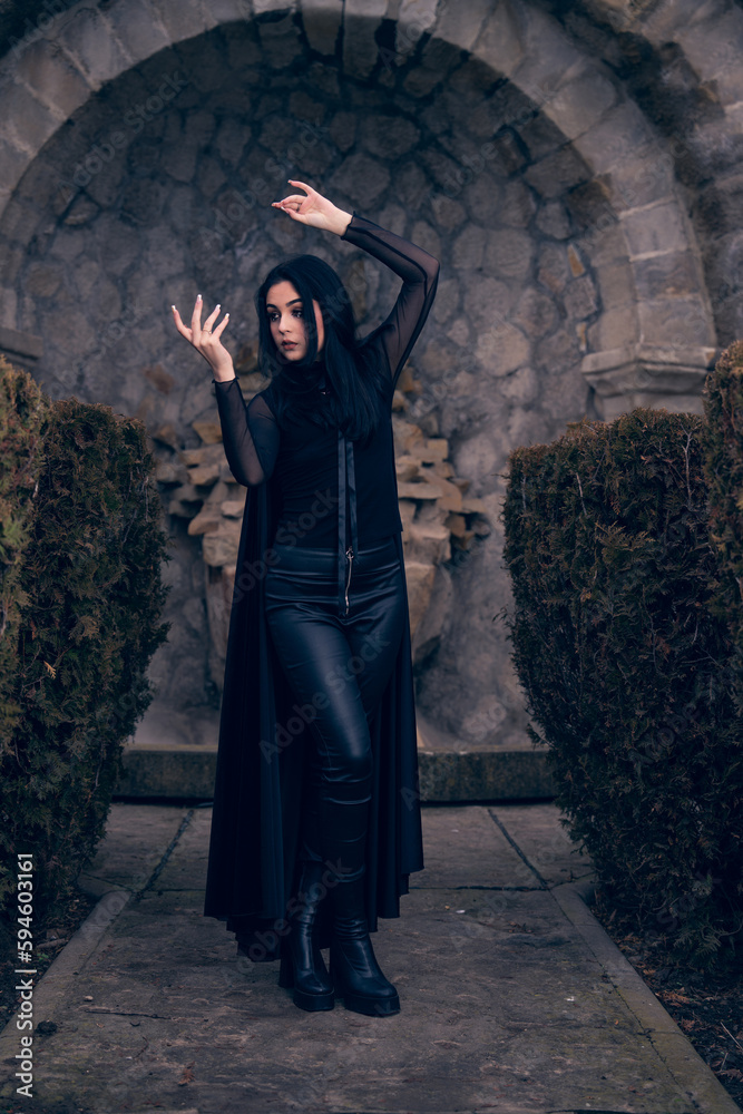 a woman in a black outfit and boots posing for a picture in front of a stone wall and a stone archway, a character portrait, gothic art