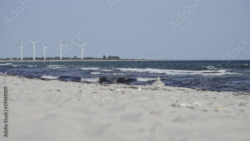 A piece of beach with crashing waves and a sandcastle to be found in Sønderborg, Denmark. In the backround wind wheels. A slow motion shot. 