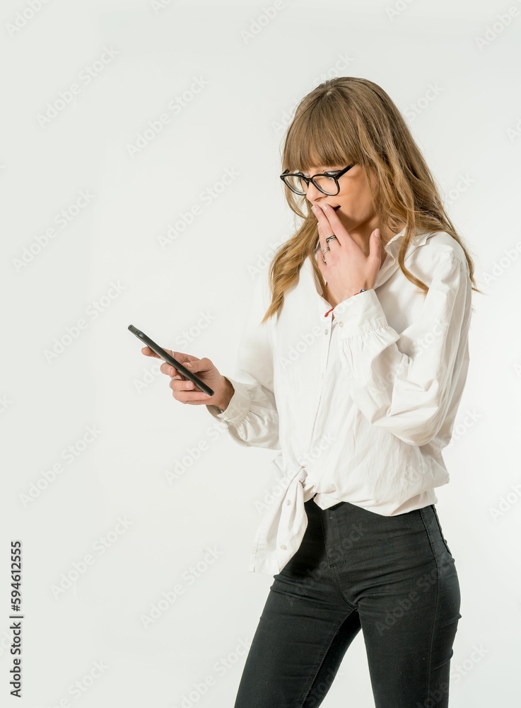 woman wearing glasses looking at her phone while standing against a white background woman wearing glasses looking at her phone while standing against a white background