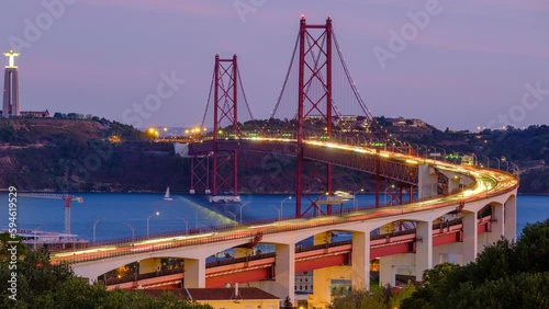 Time-lapse from Miradouro do Bairro do Alvito viewpoint of Tagus river, traffic on 25th of April Bridge and Christ the King statue in the evening twilight. Lisbon, Portugal. Zoom in effect photo