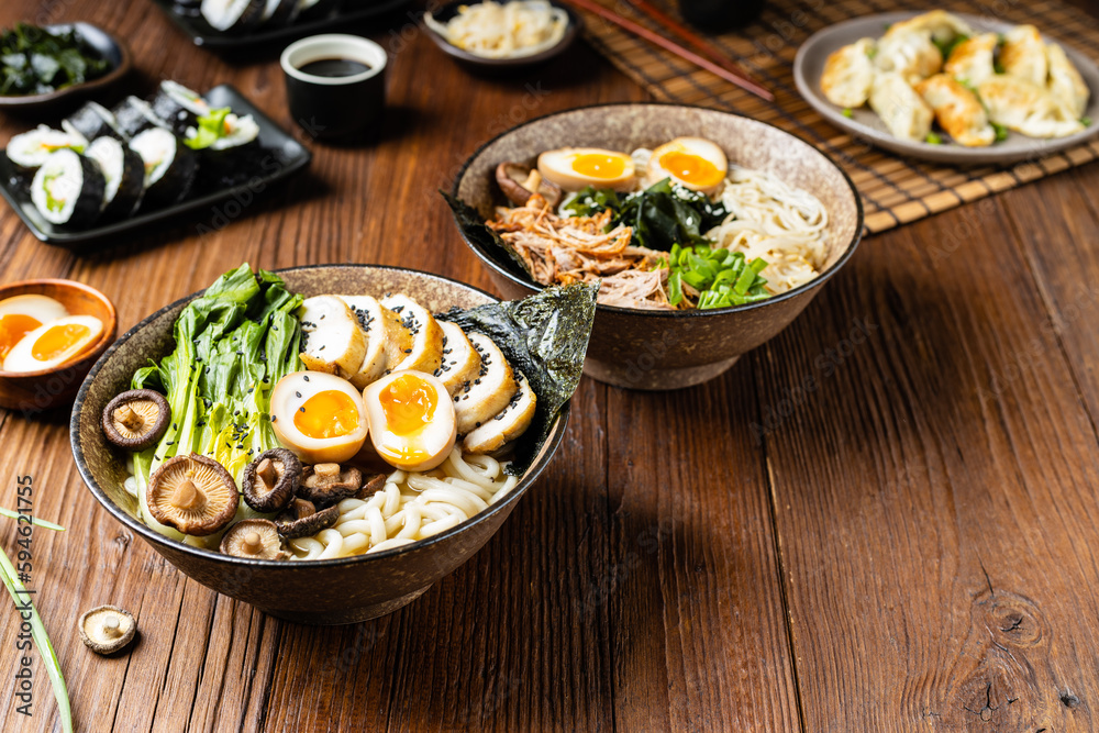 Traditional ramen with jerked pork or chicken.  With udon or ramen noodles. Served in classic bowls. Gyoza dumplings and mushrooms in the background.