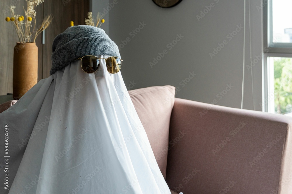 Fototapeta premium Person wearing a hat and black-rimmed sunglasses over a white cloth resembling a ghost
