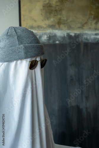 Person wearing a hat and black-rimmed sunglasses over a white cloth resembling a ghost