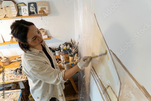 Female artist wearing protective painting gloves is focused on creating her masterpiece on a canvas photo