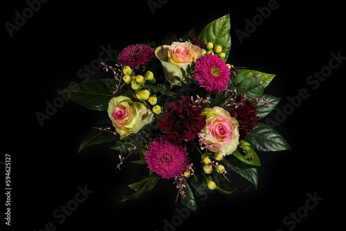 Bouquet of roses, asters and petunias decorated with leaves isolated on a black background