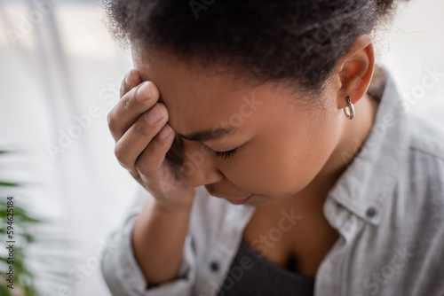 Disappointed multiracial woman with anxiety touching head at home. © LIGHTFIELD STUDIOS