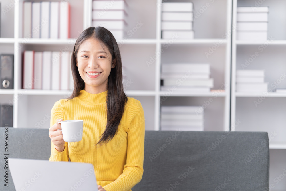 Young Asian woman sitting on sofa holding Teacup and notebook and check email, in the leaving room. Young Asian woman sitting on sofa holding Teacup and notebook and check email, in the leaving room.