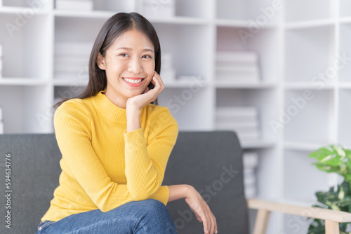 Young Asian woman sitting on sofa holding Teacup and notebook and check email, in the leaving room.