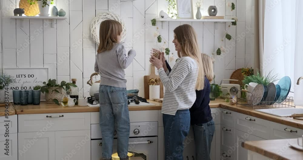 Caucasian young mother with daughters smelling cookies in jar while cooking together in kitchen at home during weekend Caucasian young mother with daughters smelling cookies in jar while cooking together in kitchen at home during weekend