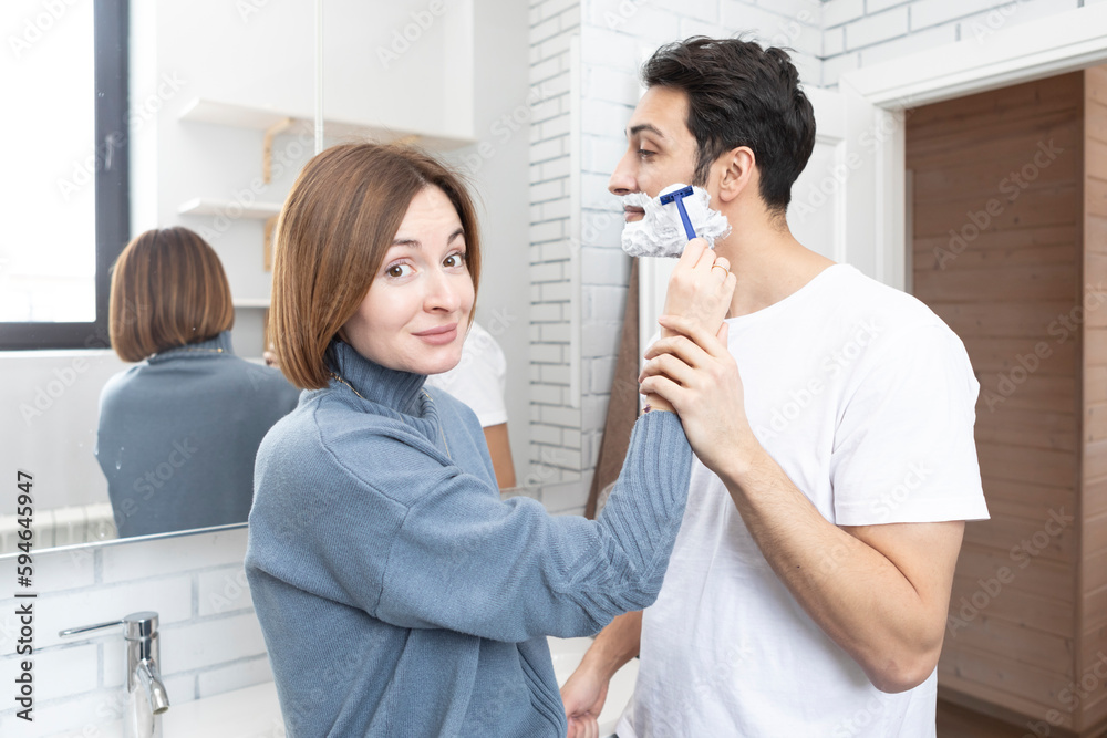 Young attractive woman helps her husband shaving in the bathroom Young attractive woman helps her husband shaving in the bathroom