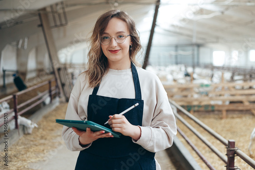Obraz na płótnie Young Caucasian Female Farm Owner with Tablet in large Livestock Stall with white Dairy Goats w salonie