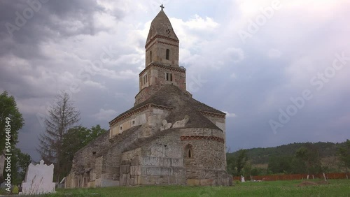 Dark clouds over the ancient Densus stone church in Romania photo