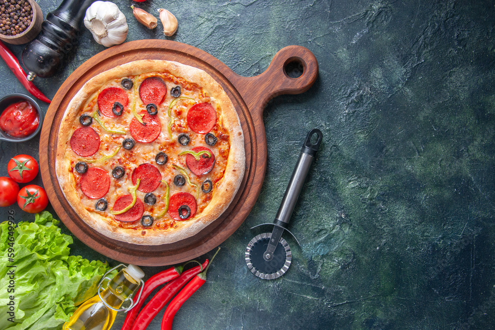 Delicious homemade pizza on wooden cutting board tomatoes garlic ketchup green bundle oil bottle pepper on dark background - obrazy, fototapety, plakaty 