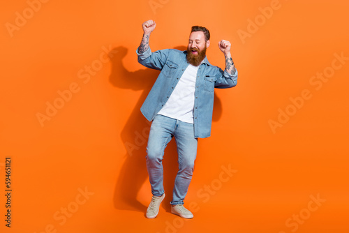 Full length photo of lucky positive man wear jeans shirt rising fists screaming yes isolated orange color background