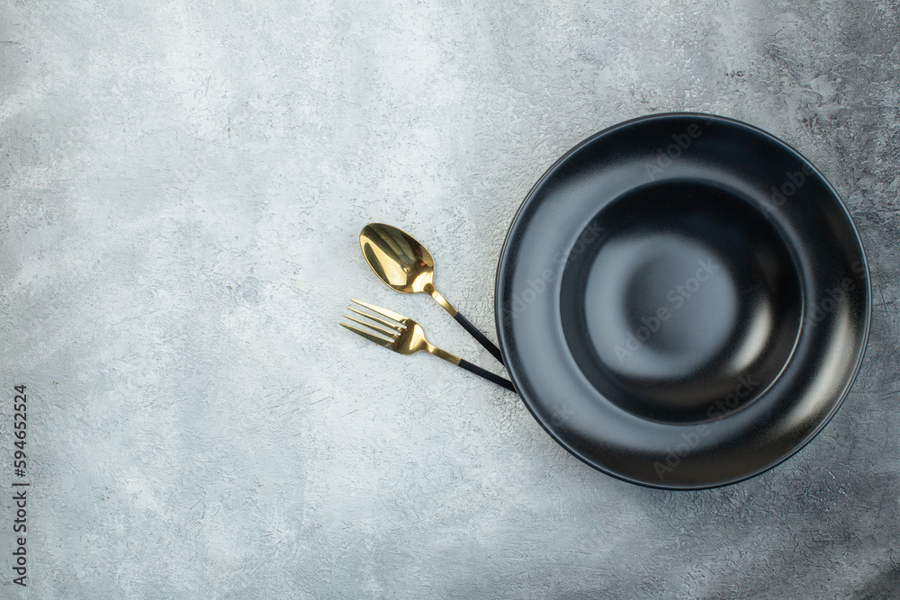 Elegant cutlery set under black dinnerware set on isolated gray ice background with free space - obrazy, fototapety, plakaty 