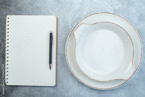 Empty white soup plates and pen on notebook on half dark light gray background with distressed surface photo