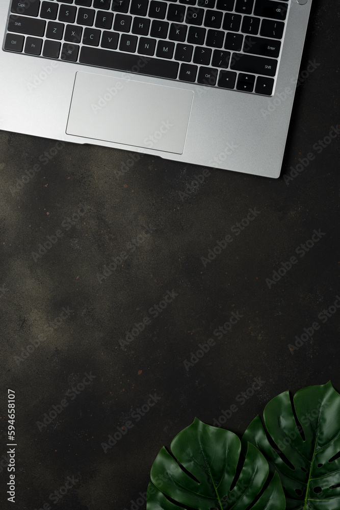 Workspace with laptop and palm leaves on black background. Flat lay
