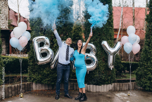 Young excited couple blowing up surprise balloon during gender reveal party. outdoor.