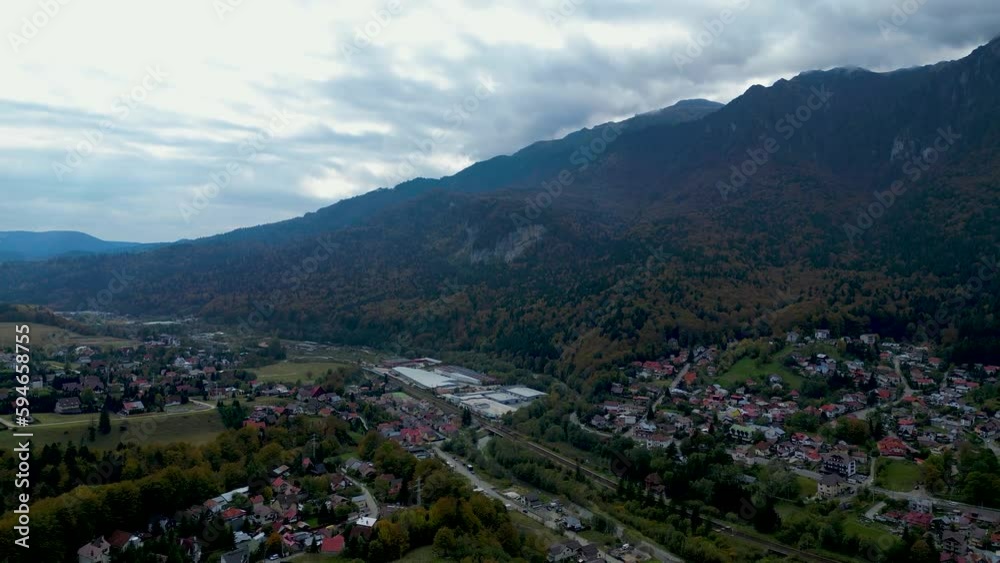 Drone filming cityscape with Suburbs houses and forest trees with green mountains under cloudy sky Drone filming cityscape with Suburbs houses and forest trees with green mountains under cloudy sky