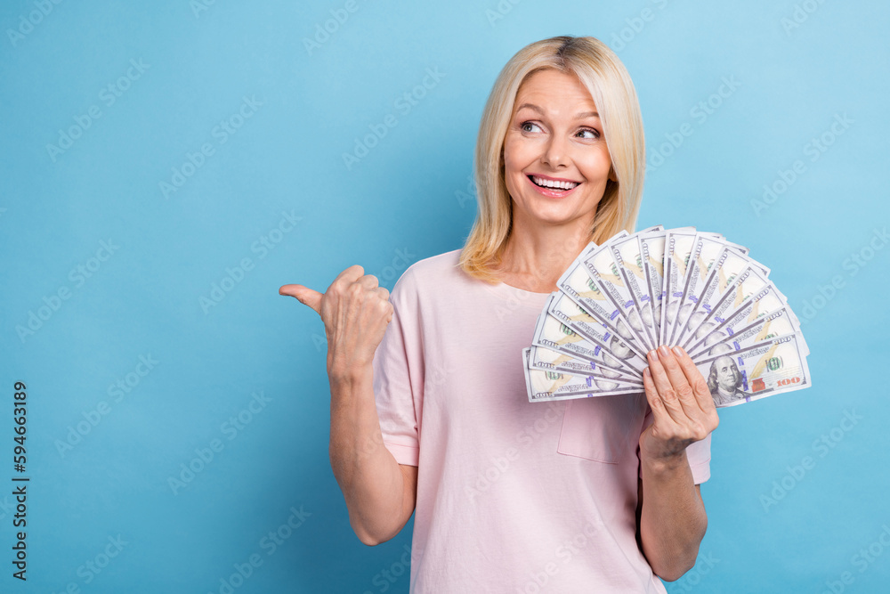 Portrait of satisfied positive senior woman wear white t-shirt look directing empty space hold dollars isolated on blue color background Portrait of satisfied positive senior woman wear white t-shirt look directing empty space hold dollars isolated on blue color background