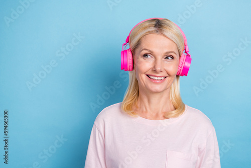 Photo of cute positive person toothy smile look empty space enjoy music earphones isolated on blue color background
