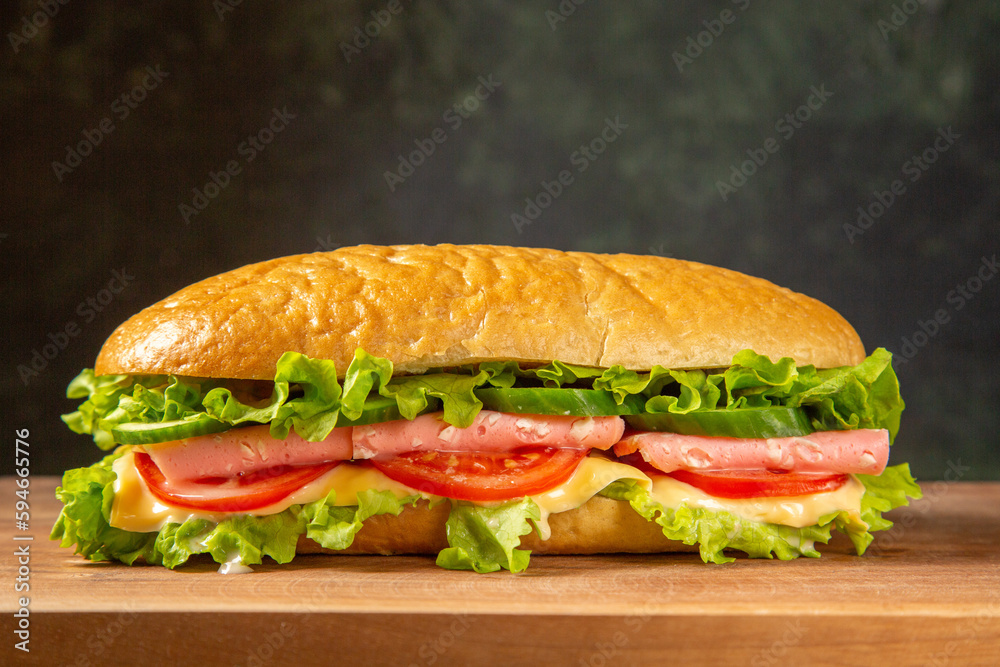 Tasty homemade sandwich on wooden cutting board on black distressed background Tasty homemade sandwich on wooden cutting board on black distressed background