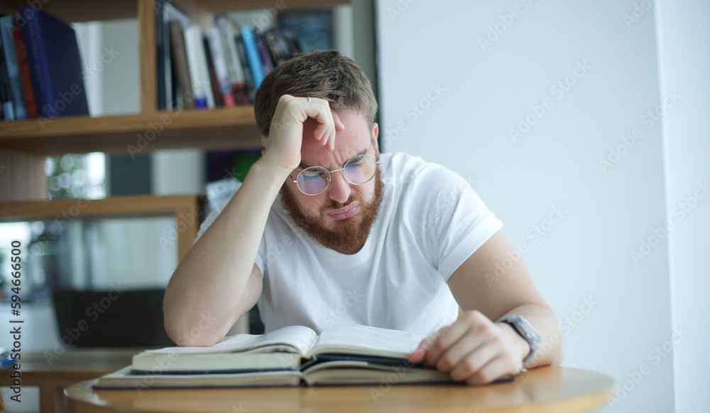 Portrait of tired overworked guy, exhausted young man in glasses college or university student is study hard in library, prepare to exam, lesson Portrait of tired overworked guy, exhausted young man in glasses college or university student is study hard in library, prepare to exam, lesson