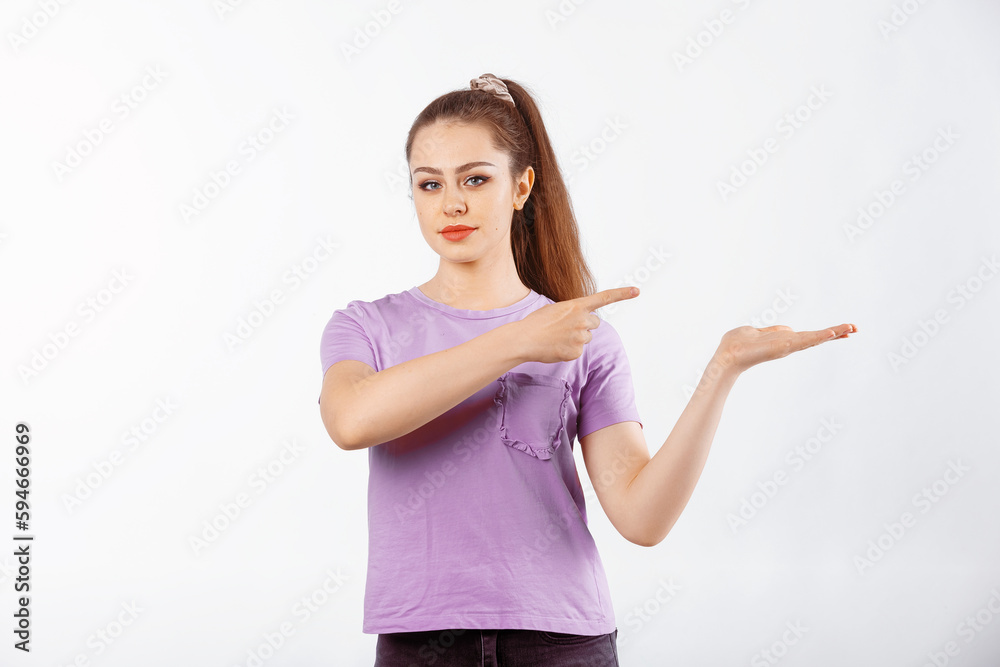 Happy young woman with long hair points finger at banner, shows great promo offer aside, stands in casual t shirt over white background Happy young woman with long hair points finger at banner, shows great promo offer aside, stands in casual t shirt over white background
