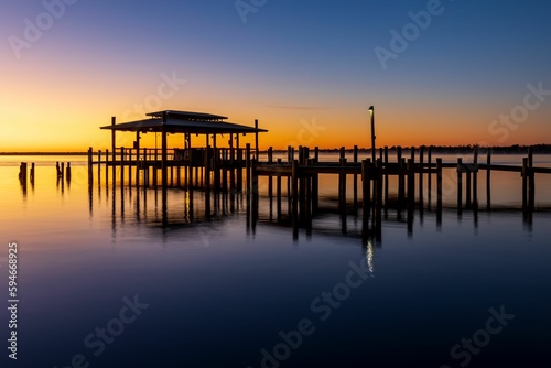 Calm sunrise over a wooden structure on on the water on a misty morning © Jason159/Wirestock Creators