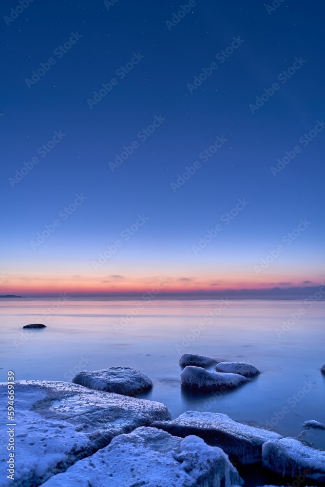 Vertical shot of an idyllic frozen rocky shore with blue and pink sunset in the background