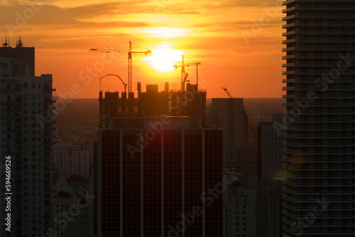 Aerial view of new developing residense in american urban area at sunset. Tower cranes at industrial construction site in Miami, Florida. Concept of housing growth in the USA