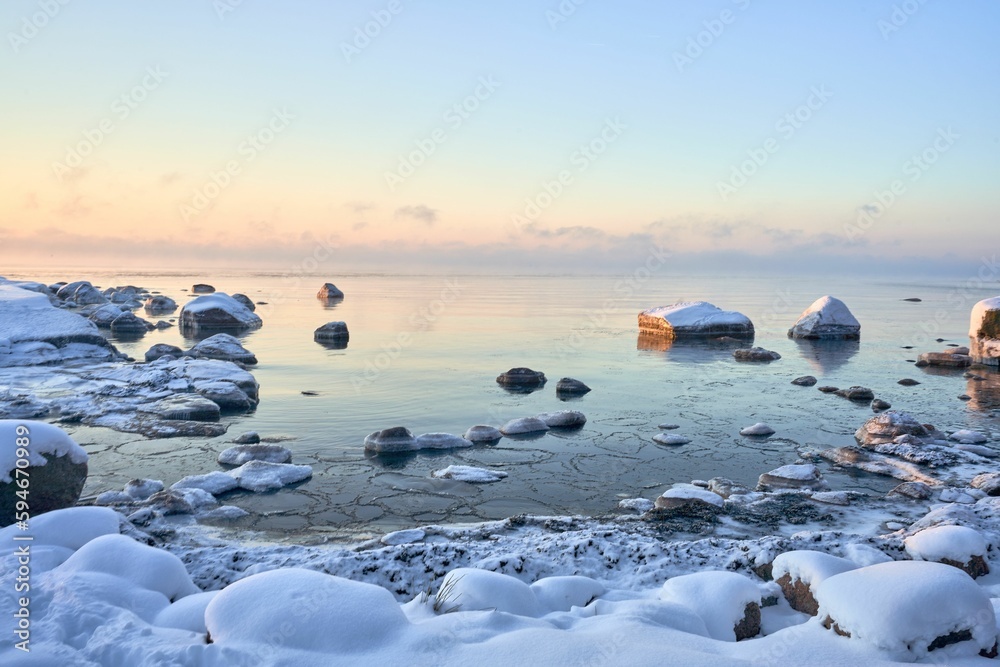 Tranquil shoreline in winter, with snow-covered rocks and a partially frozen surface of the sea Tranquil shoreline in winter, with snow-covered rocks and a partially frozen surface of the sea