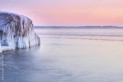 Idyllic frozen huge rock in the middle of the sea with pink sky on the horizon