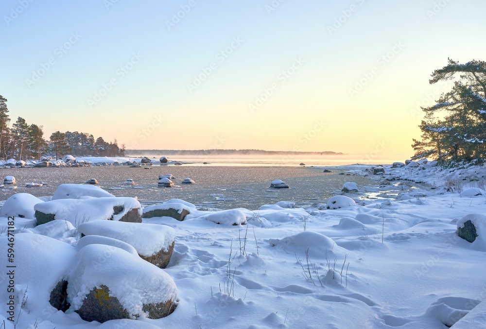 Tranquil shoreline in winter, with snow-covered rocks and a partially frozen surface of the sea