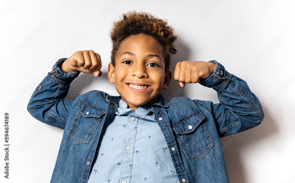 Portrait of a cute 5-6 year old boy with dark skin and afro hair posing on a white background. The child makes the positive gesture showing the 2 biceps. Concept of proud and confident children. Portrait of a cute 5-6 year old boy with dark skin and afro hair posing on a white background. The child makes the positive gesture showing the 2 biceps. Concept of proud and confident children.