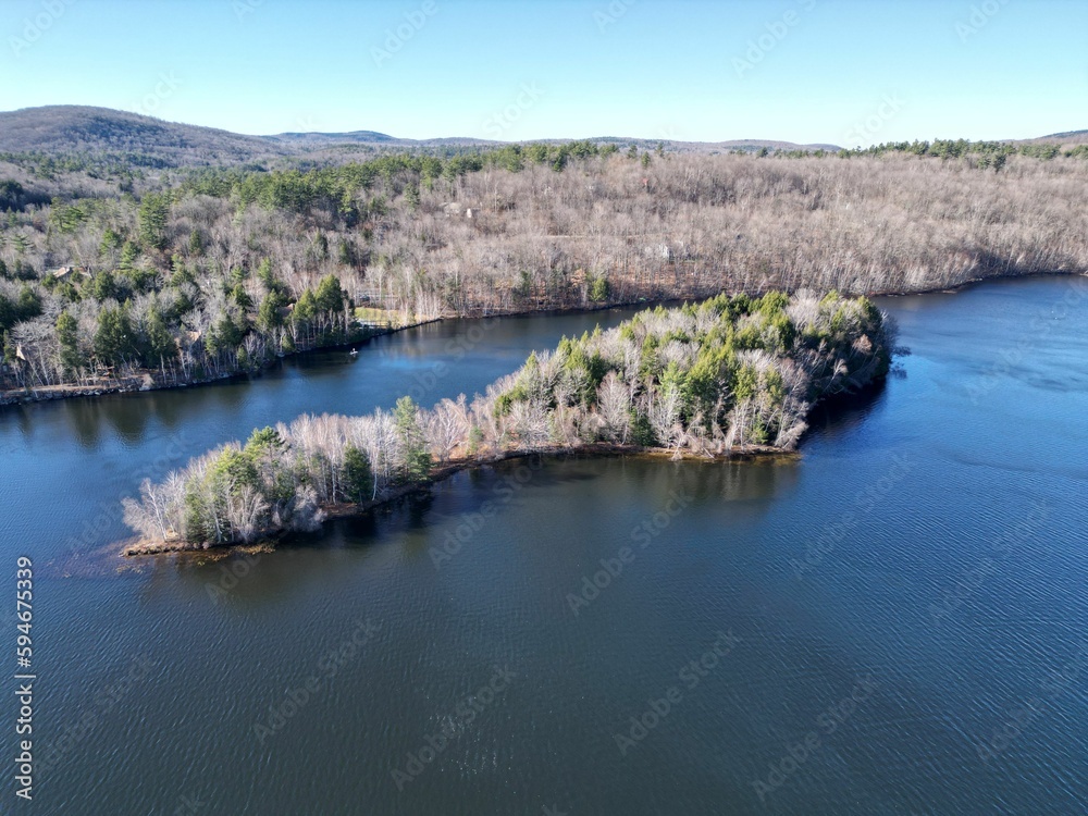 Areal view of a tranquil lake in New Hampshire, surrounded by lush green trees set in a wooded area