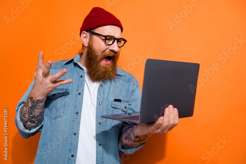 Photo of angry screaming man wear jeans shirt spectacles having working problem gadget empty space isolated orange color background