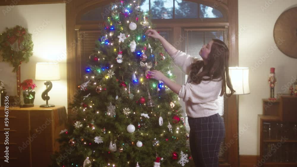 Beautiful girl decorating a huge Christmas tree with garlands in the living room for the new year Beautiful girl decorating a huge Christmas tree with garlands in the living room for the new year