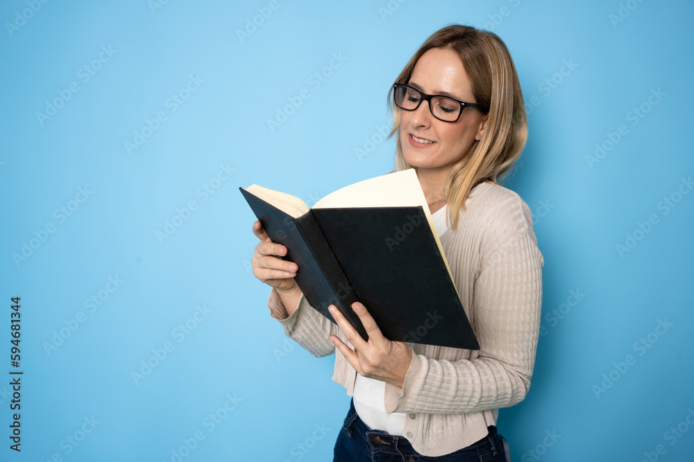 Portrait of a smiling young caucasian woman reading a book isolated over blue background Portrait of a smiling young caucasian woman reading a book isolated over blue background
