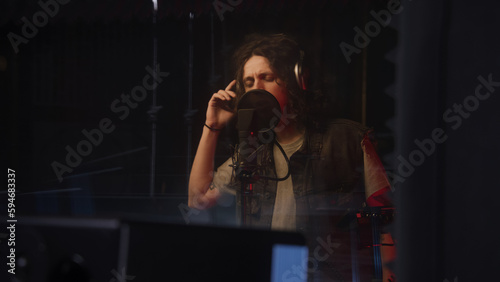 Male singer, artist, performer records new song in soundproof room. Musician in headphones sings into the professional microphone. Modern sound recording studio equipment. Music production concept.