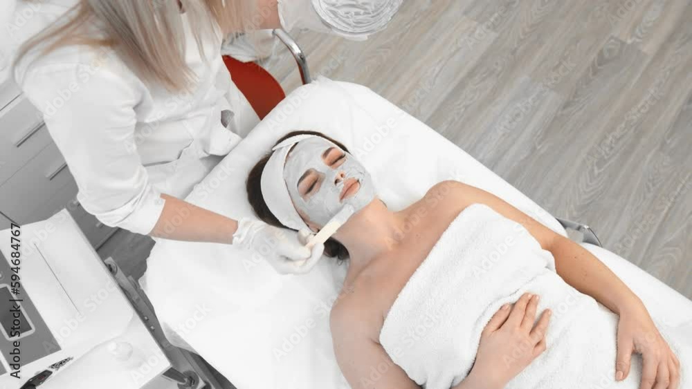 In a beauty salon, a client receives a facial treatment from a beauty therapist. Client enjoys a pampering spa experience in a serene and tranquil environment. The therapist applies a hydrating mask