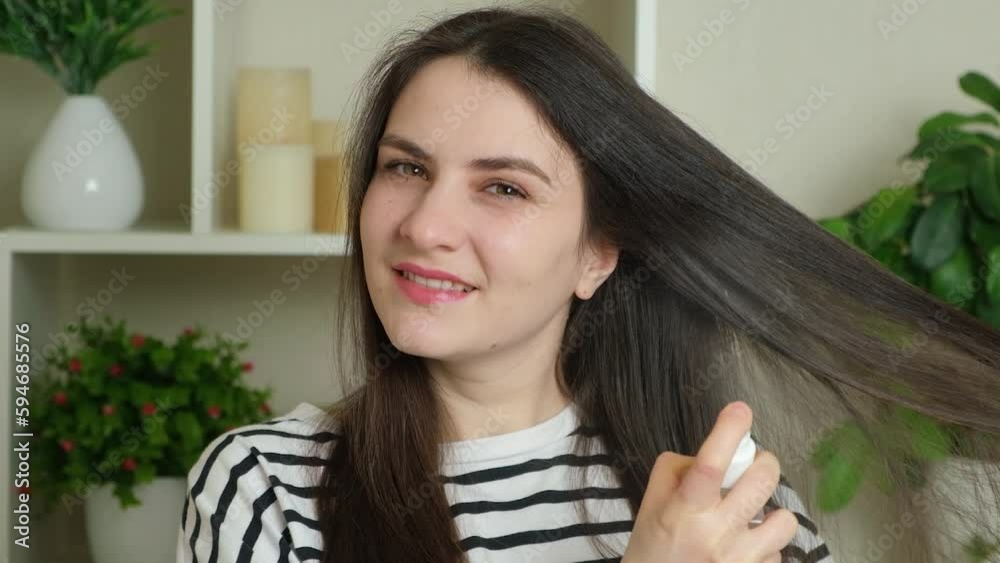A brunette woman with long hair applies tonic spray to her hair. A brunette woman with long hair applies tonic spray to her hair.