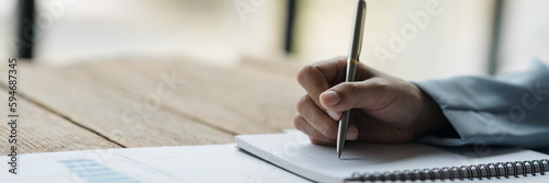 Hand shot of a businesswoman, investor, insurance salesman taking notes in a notebook on earnings performance graphs. Financial charts in real estate projects at office desks.